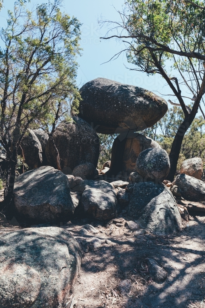 vertical shot of rocks stacked on top of each other with trees at the back on a sunny day - Australian Stock Image