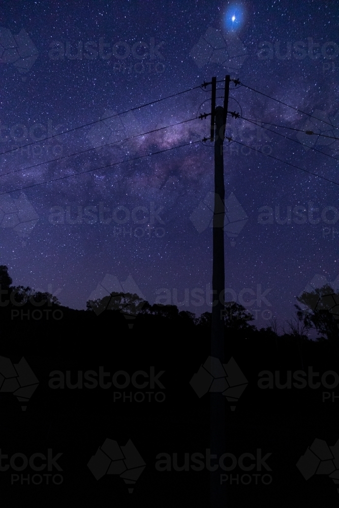 vertical shot of some silhouette of trees, bushes and electric post of wires at dawn with stars - Australian Stock Image