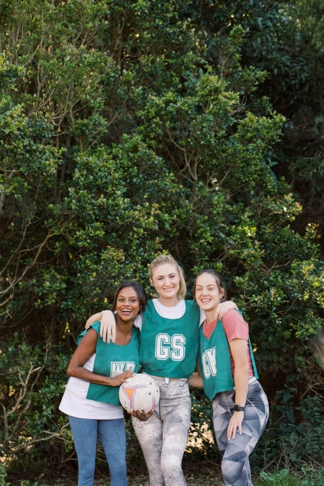 vertical shot of three young sporty women posing outdoors with one holding a net ball - Australian Stock Image