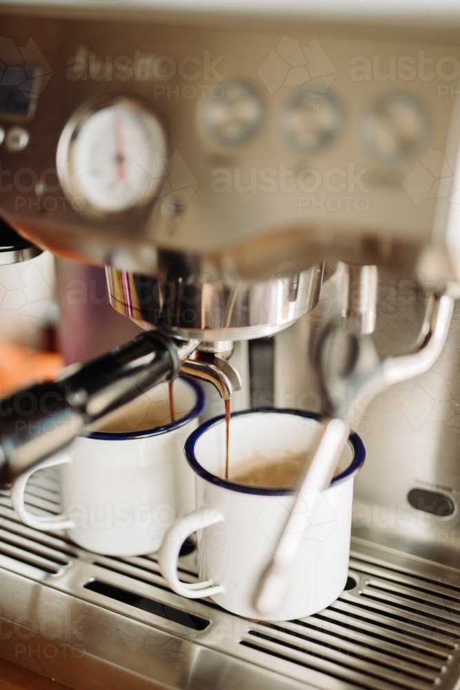 Vertical shot of two white cups being served with a brewed coffee on a coffee maker - Australian Stock Image