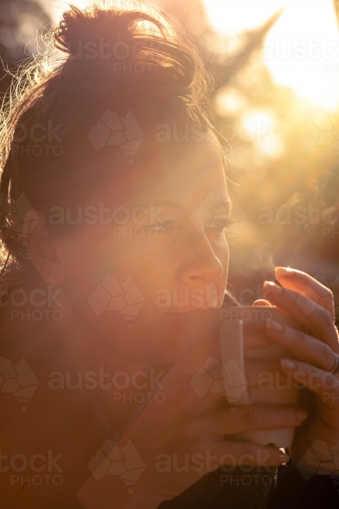 vertical shot of woman with a messy bun hairstyle looking from a far sipping a drink from a mug - Australian Stock Image