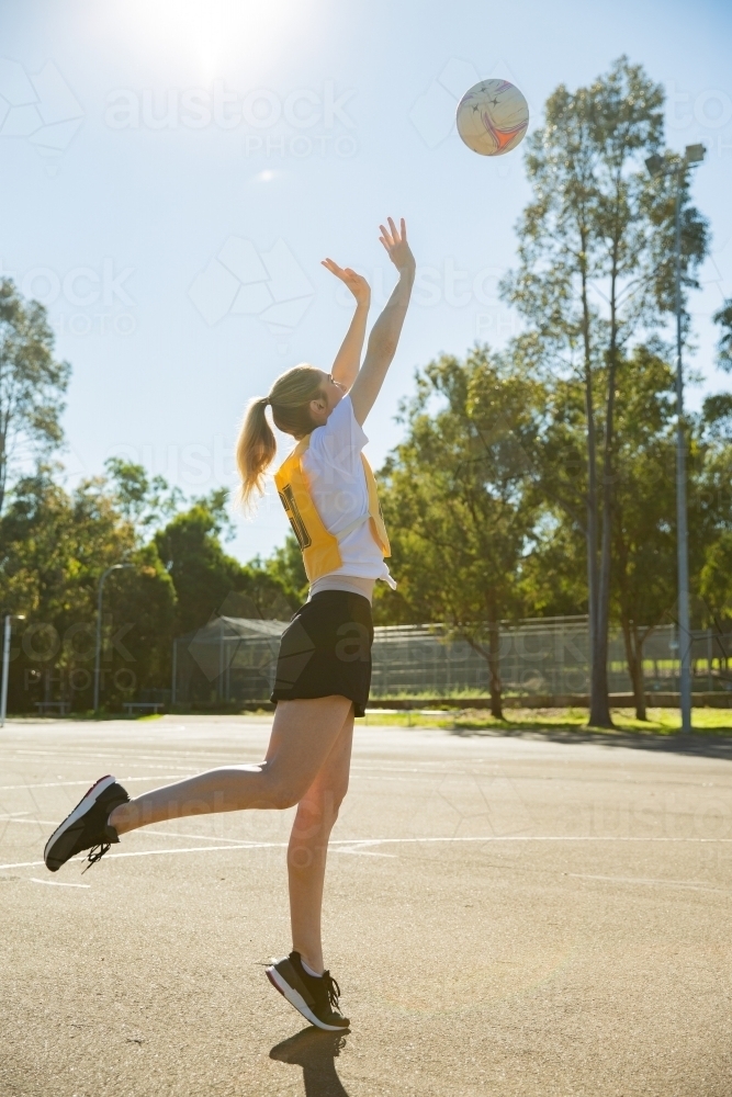 vertical shot of young woman in sporty clothes throwing a ball in the air with one foot raised - Australian Stock Image