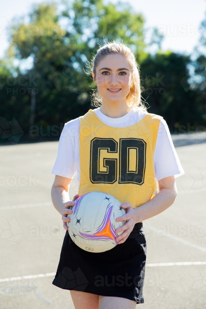 vertical shot of young woman wearing yellow and black sports wear holding a net ball with two hands - Australian Stock Image