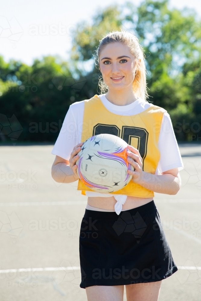 vertical shot of young woman wearing yellow and black sports wear holding a net ball with two hands - Australian Stock Image