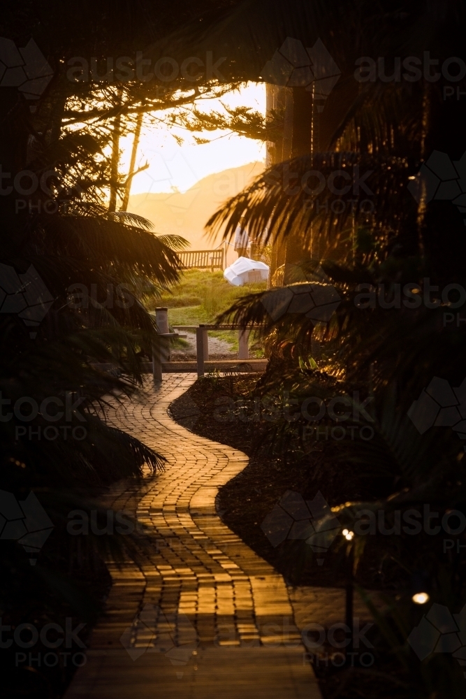 vertical silhouette shot of a sunset with tiled walkway leaves and wooden chair outside - Australian Stock Image