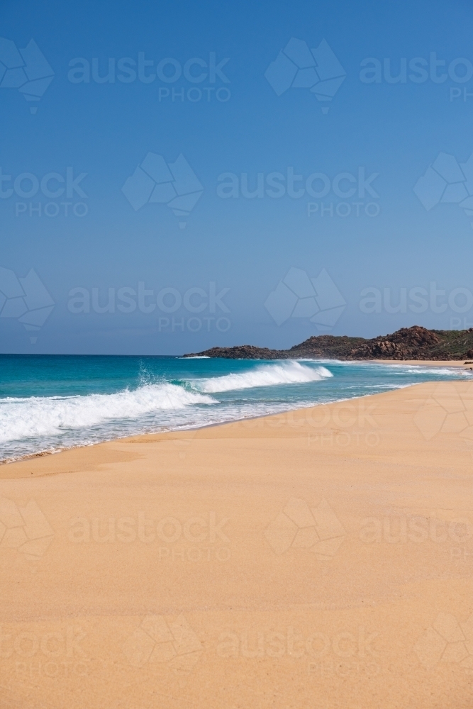 Vertical view looking along sandy beach with waves towards a headland - Australian Stock Image