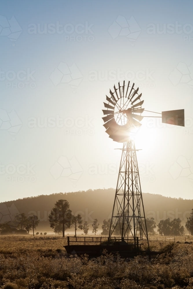 Vertical windmill with sun flare behind on farm in morning light - Australian Stock Image