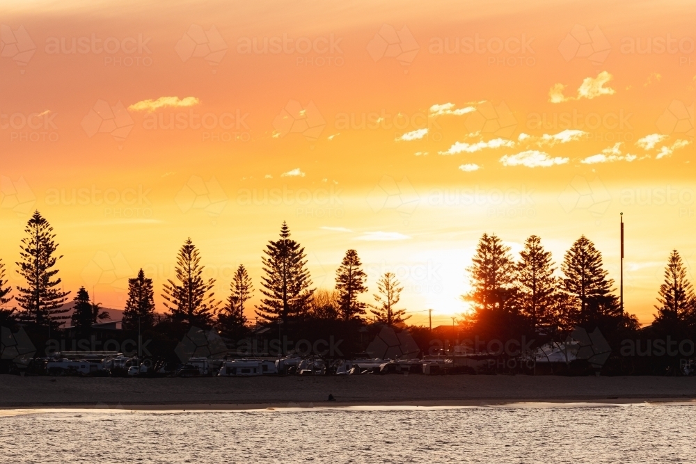 Vibrant orange sunset over caravan park at Stockton NSW with view across the water - Australian Stock Image