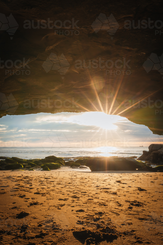 Vibrant sunflare illuminating inside of beach cave at sunrise - Australian Stock Image