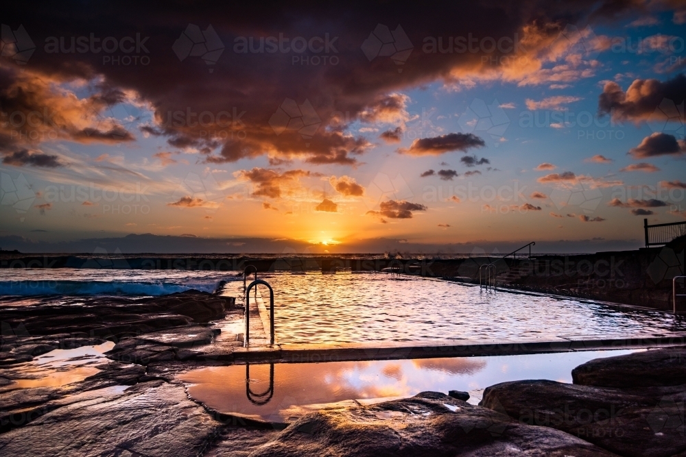 Vibrant sunrise colours in the sky over the ocean pool - Australian Stock Image