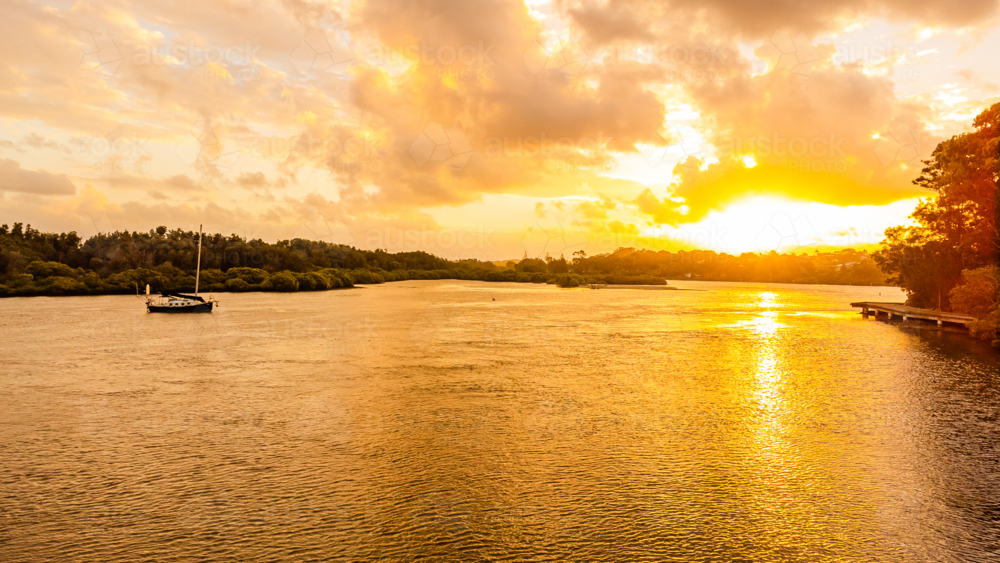 vibrant sunset over river estuary with sailing boat - Australian Stock Image