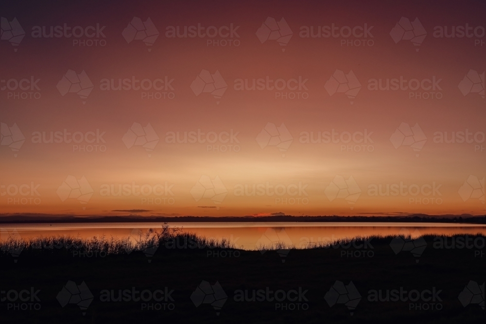 Vibrant sunset sky over Tuggerah Lake from Canton Beach on the Central Coast in Toukley, NSW - Australian Stock Image