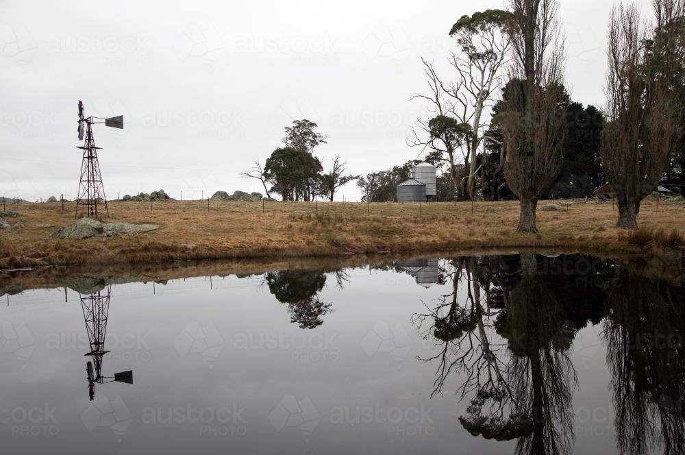 View across dam to windmill and farm buildings - Australian Stock Image