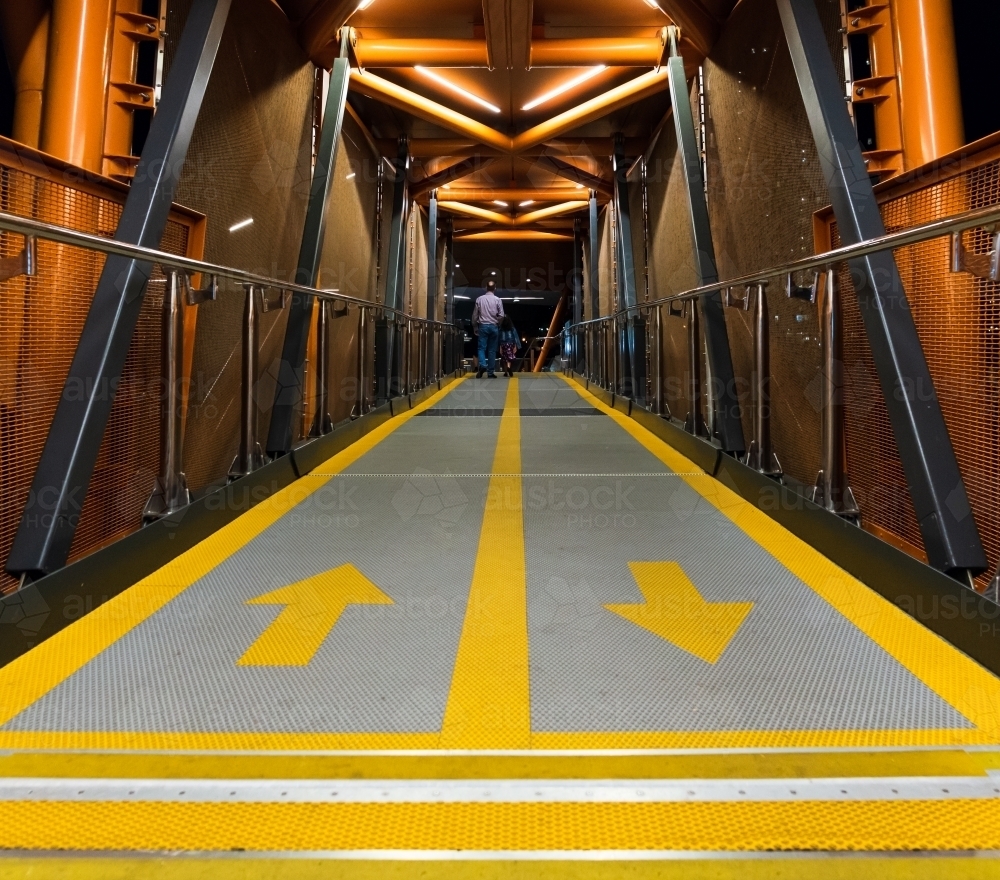 view along an enclosed walkway to a person with yellow lines and arrows - Australian Stock Image