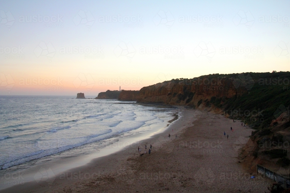 View along beach towards lighthouse at dusk - Australian Stock Image
