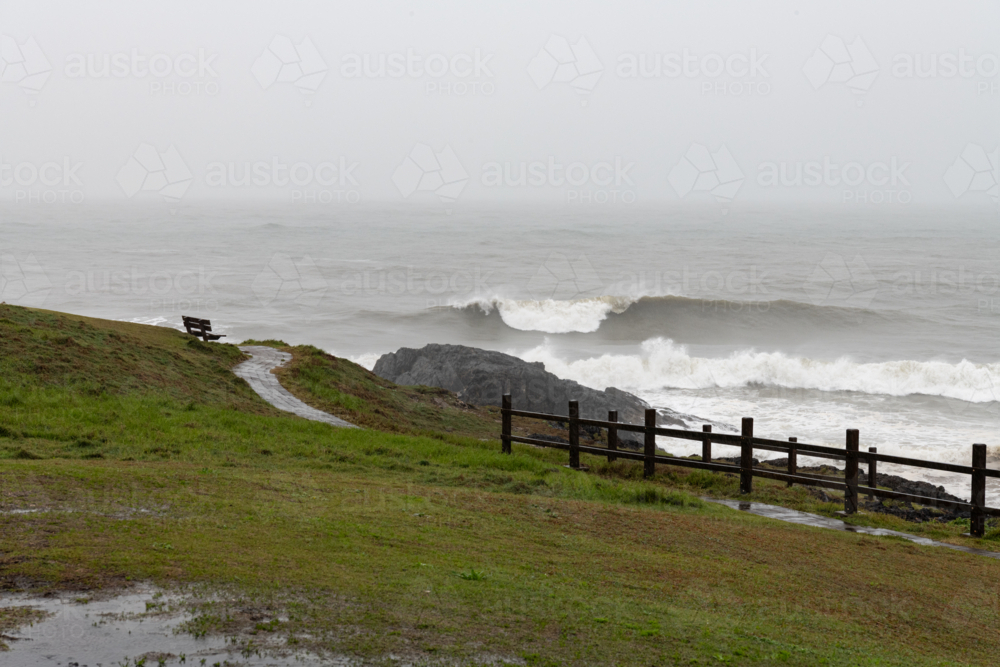 View from a headland of waves breaking in a grey ocean in rainy wild weather - Australian Stock Image