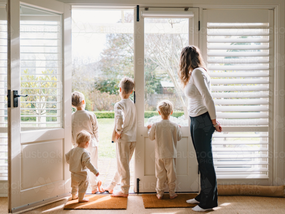 View from behind of young boys standing in the doorway with mum looking through glass door - Australian Stock Image