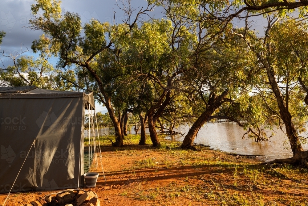 View of a campsite beside  an outback lagoon in early morning golden light - Australian Stock Image
