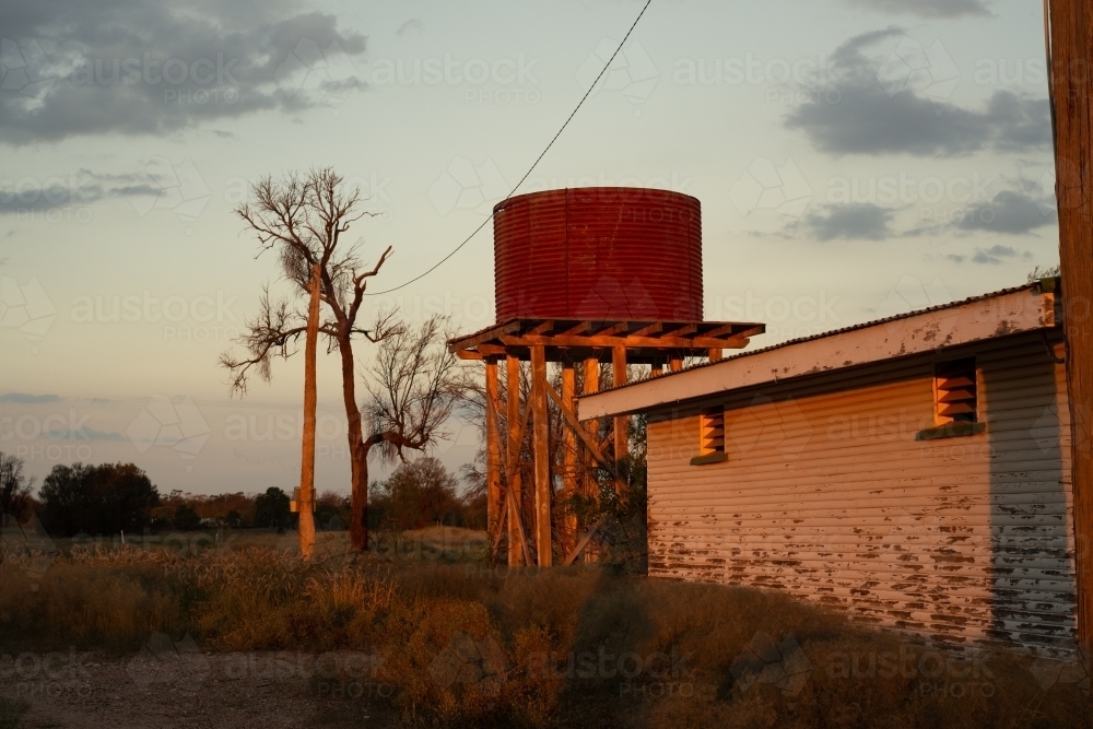 View of an old building with a rusted tank on stand in beautiful late afternoon light - Australian Stock Image