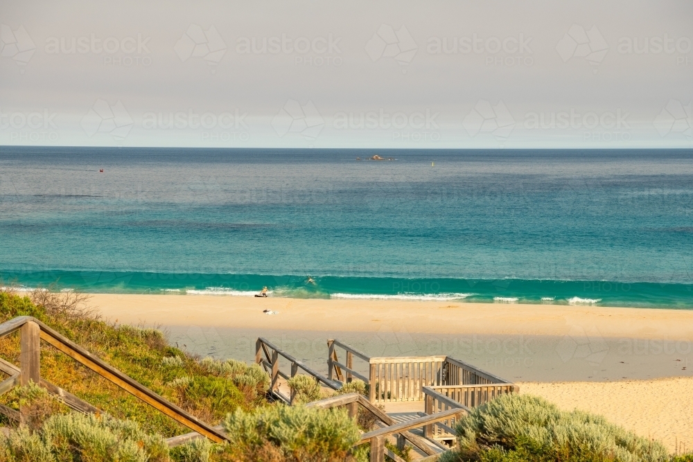 View of beach with people in water from upper boardwalk and staircase - Australian Stock Image