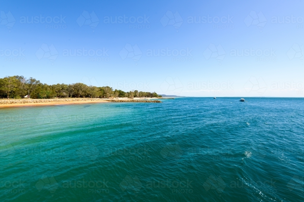 View of blue green water and island beach with clear blue sky - Australian Stock Image