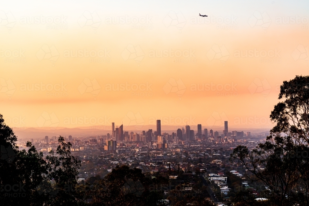 View of Brisbane City skyline with colourful orange smoke haze and airplane  in the sunset - Australian Stock Image