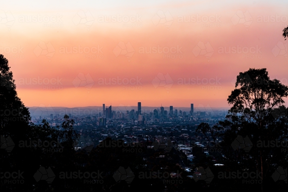 View of Brisbane City skyline with colourful orange smoke haze in the sunset - Australian Stock Image