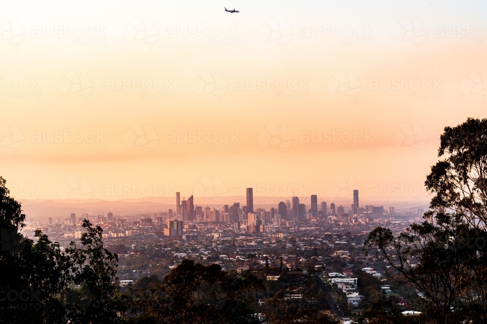 View of Brisbane City skyline with colourful smoke haze and airplaine in the sunset - Australian Stock Image