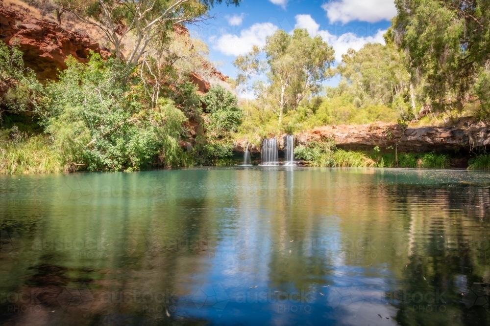 View of calm waters and a clear reflection in front of a waterfall - Australian Stock Image