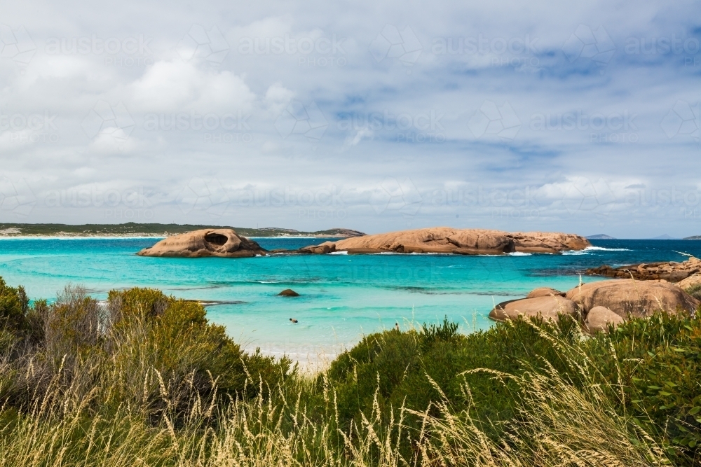 View of cove with turquoise water and colourful rocky islands and shrubs in the foreground. - Australian Stock Image