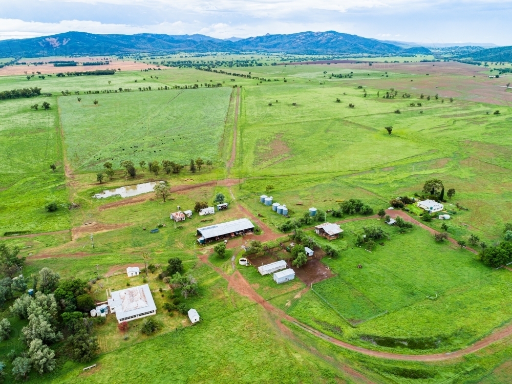View of distant farm home area with house and sheds among green paddocks - Australian Stock Image