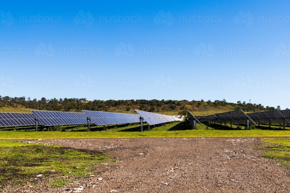 View of gravel road leading to solar panels in rural setting with clear blue sky - Australian Stock Image