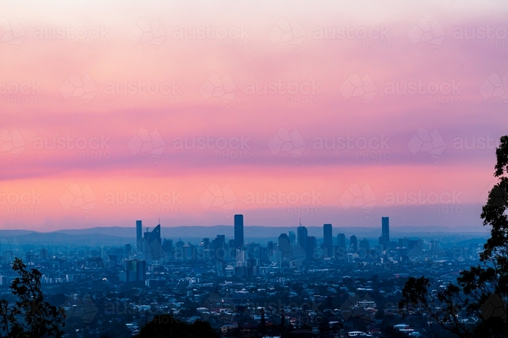 View of hazy Brisbane City skyline with colourful purple and pink smoke haze in the sunset - Australian Stock Image