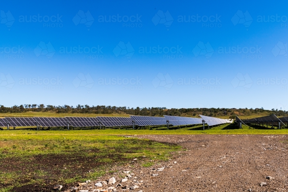 View of large scale solar farm in rural setting with gravel road and clear blue sky - Australian Stock Image