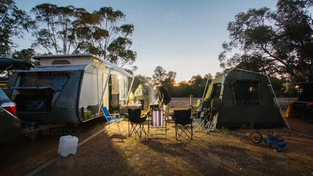 View of people cooking outside their caravan campsite at sunset - Australian Stock Image