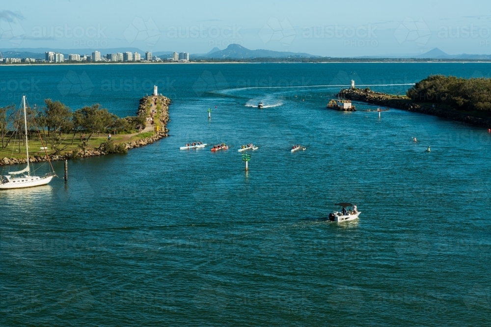 View of river mouth with outrigger canoes training, high rise and mountains in the distance - Australian Stock Image