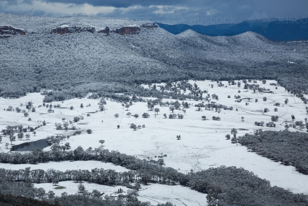 View of snow-covered paddocks and forested escarpment - Australian Stock Image