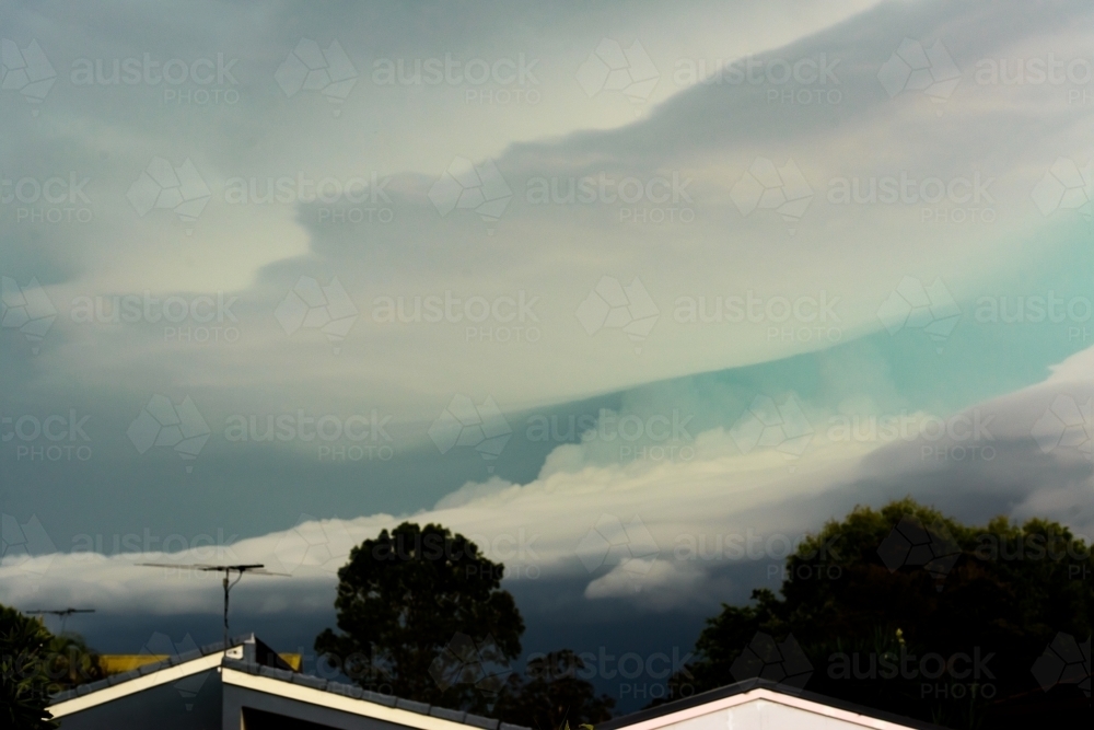 View of storm clouds with green band of hail over suburban rooftops - Australian Stock Image