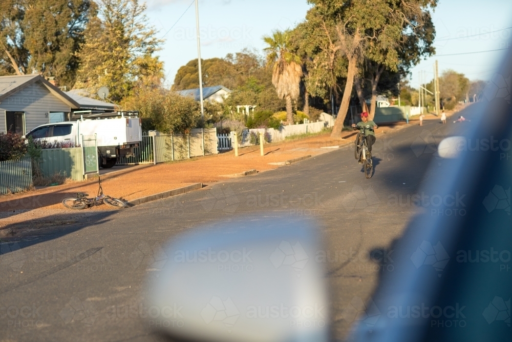 view of street with blurred car in foreground and boy doing wheelie on bike - Australian Stock Image