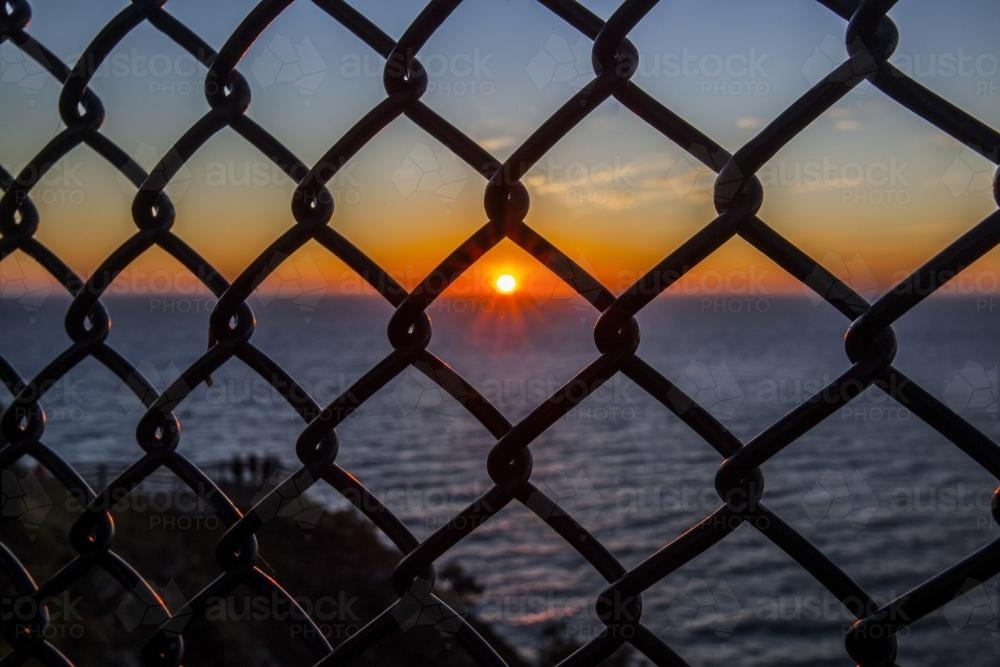 view of sunrise over the ocean through a wire fence - Australian Stock Image