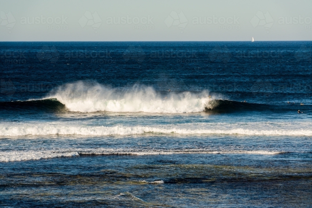 View of surfers with a wave breaking off Surfers Point - Australian Stock Image