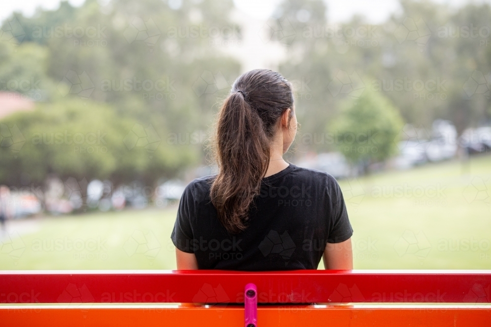 View of woman sitting at a park bench looking out from behind - Australian Stock Image