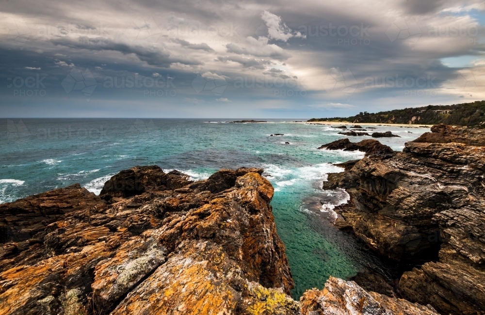 View over Mystery Bay with dramatic rocks in foreground and stormy sky - Australian Stock Image