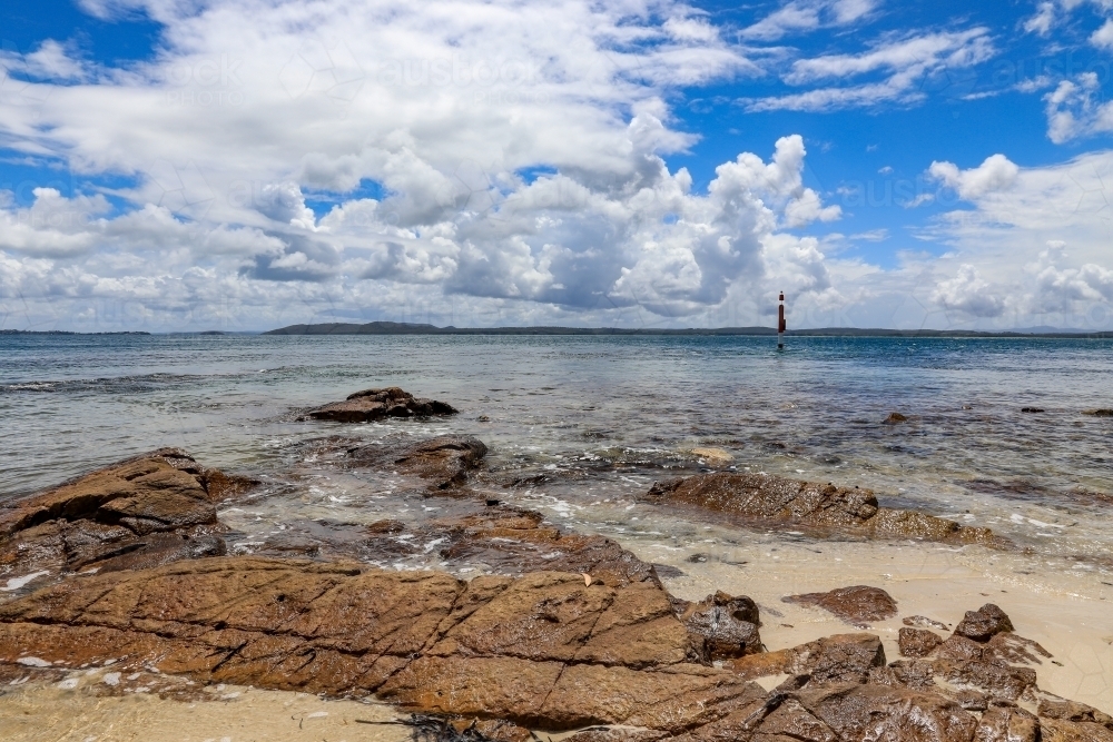 View over rocky coastline against ocean and blue cloudy sky - Australian Stock Image