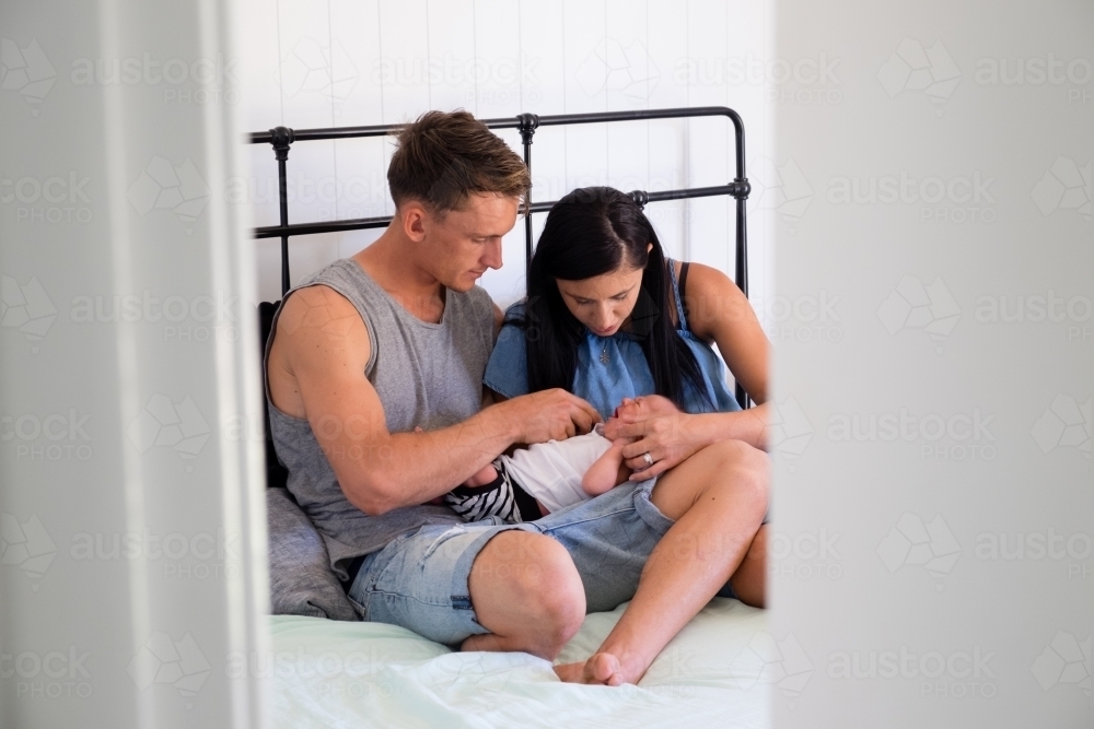 View through door of new parents on their bed comforting a newborn baby - Australian Stock Image