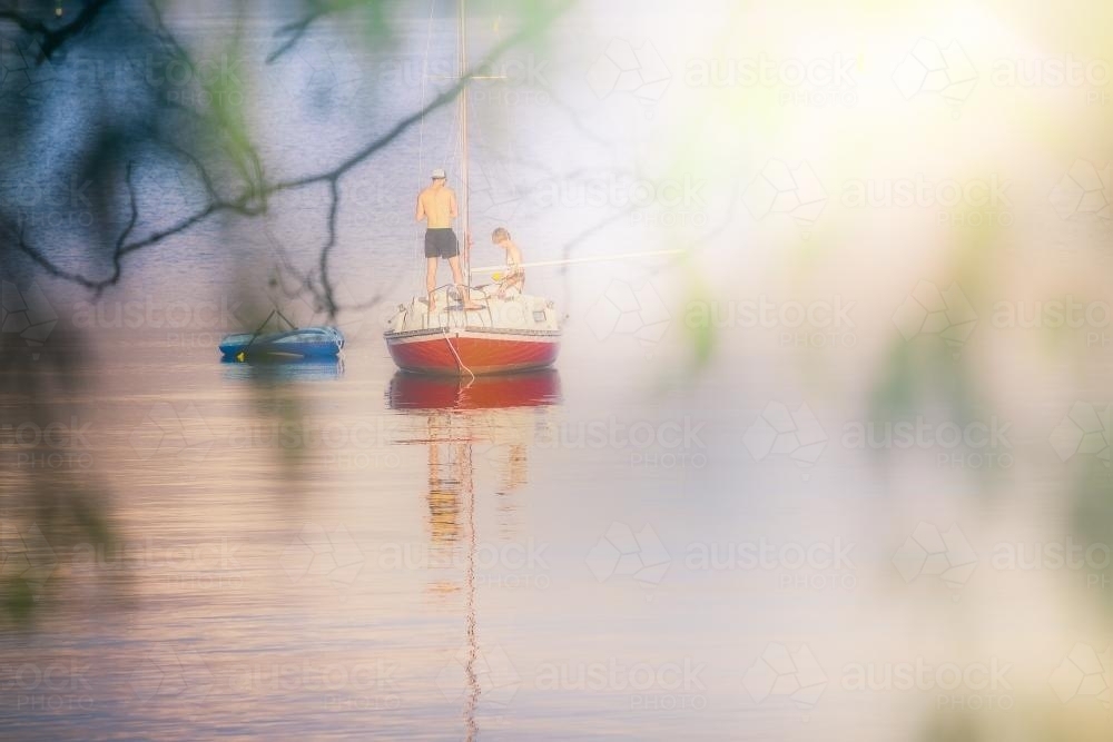 View through trees of people on small sailing boat on the Swan River - Australian Stock Image