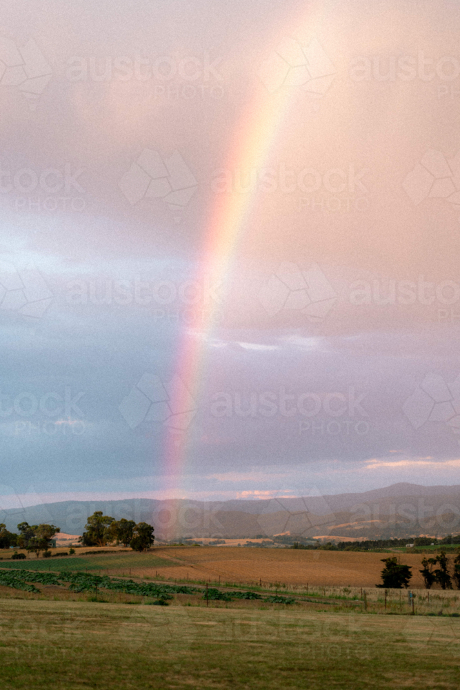 Vivid rainbow arching across moody sky of the countryside - Australian Stock Image