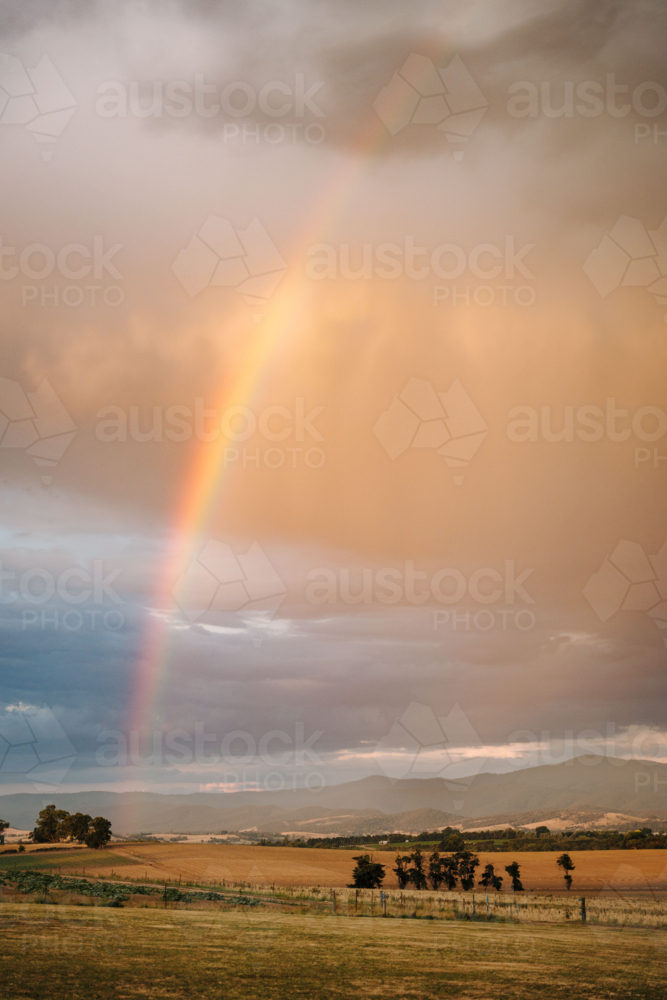 Vivid rainbow arching across moody sky of the countryside - Australian Stock Image