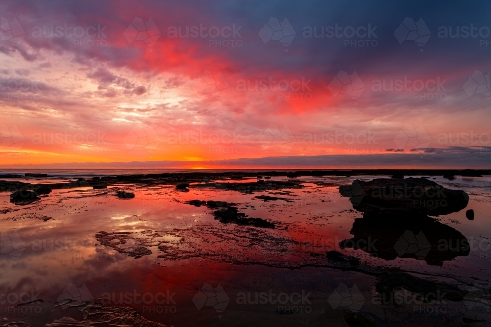 Vivid reflections of sunrise on coastal seascape at low tide - Australian Stock Image
