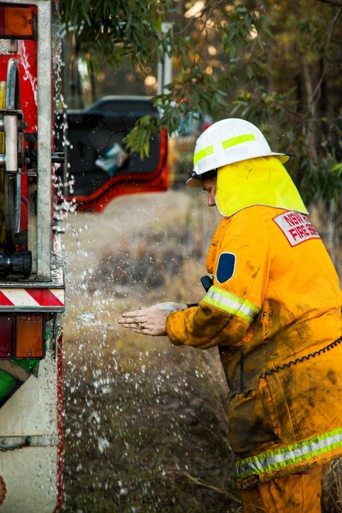 Volunteer firefighter woman washing her hands after fire in overflow water from firetruck - Australian Stock Image
